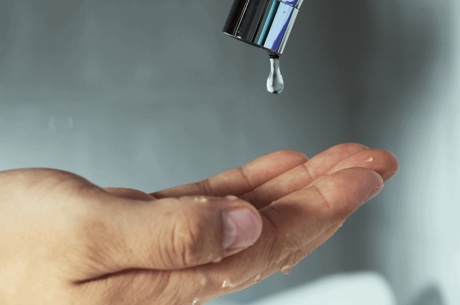 Water droplet falling from faucet onto right open hand