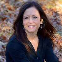 Headshot of Andria Corso in the woods, wearing dark blue shirt and has dark hair