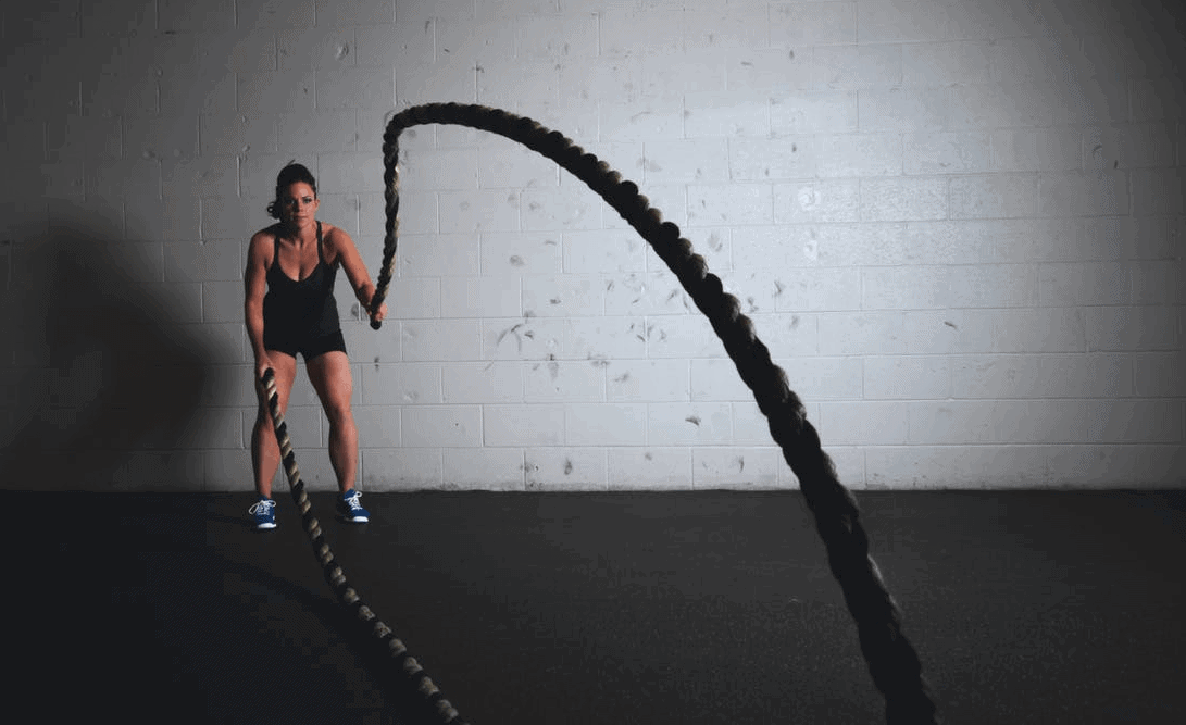 women mid battle rope workout inside gym